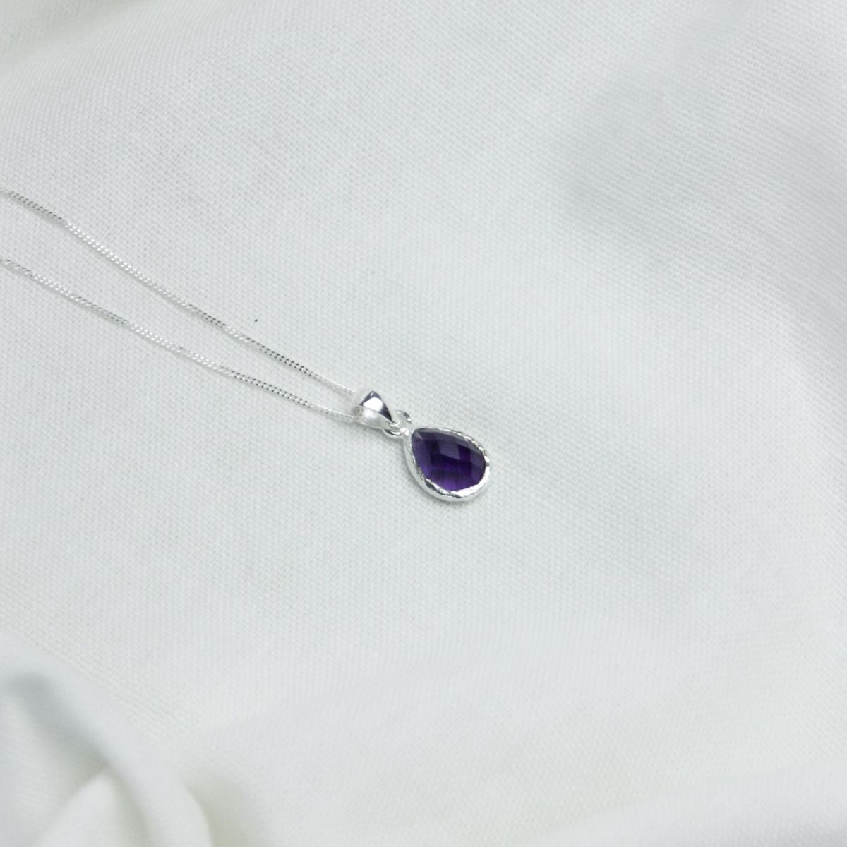 a purple pendant necklace on a white cloth