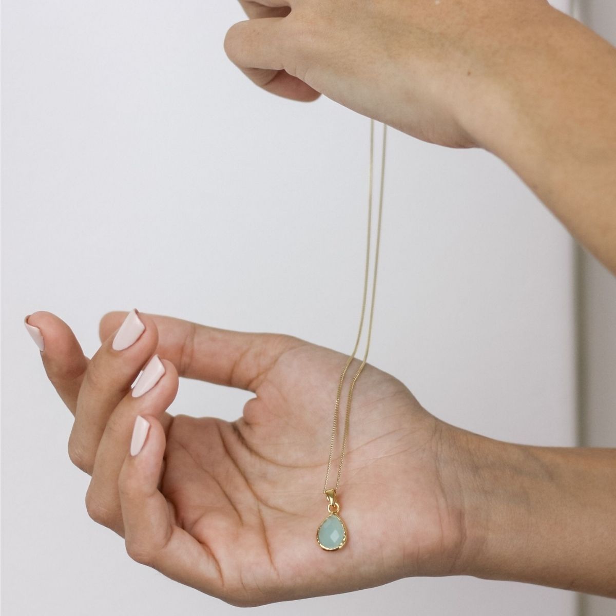 a woman holding a blue pendant necklace in her hand