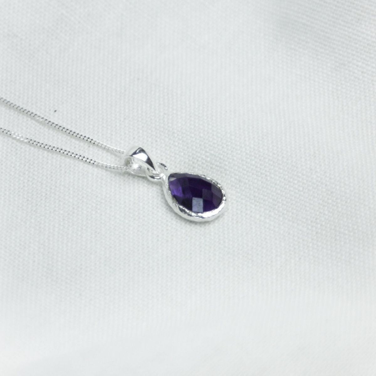 a purple pendant necklace on a white cloth