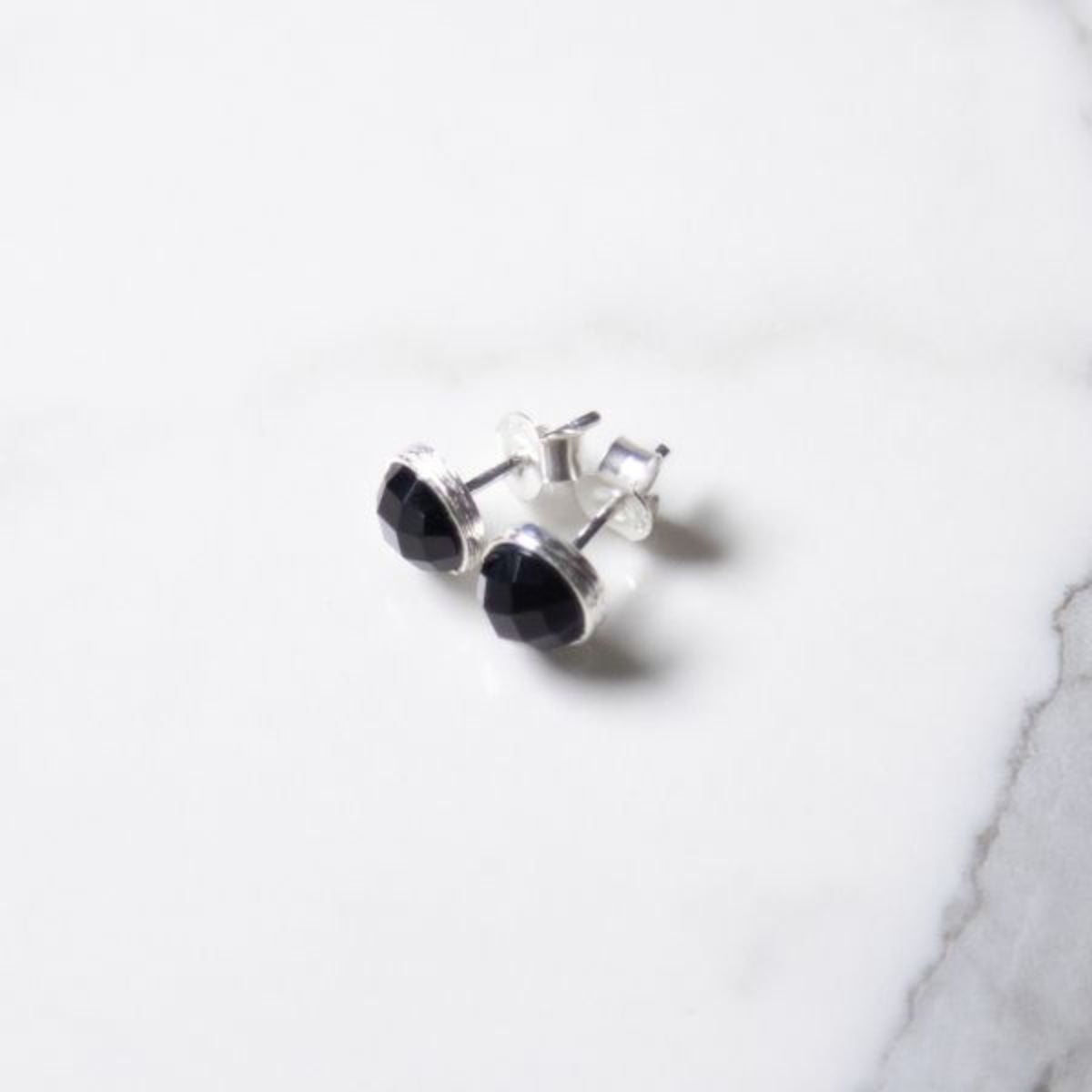two black onyx stud earrings on a marble background