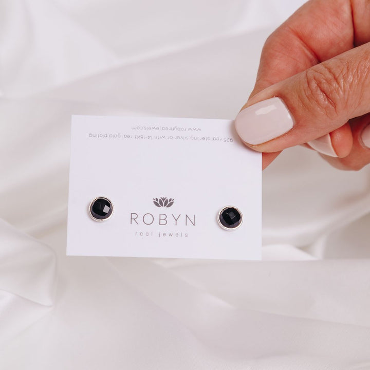 a woman holding a two black onyx studs on a card