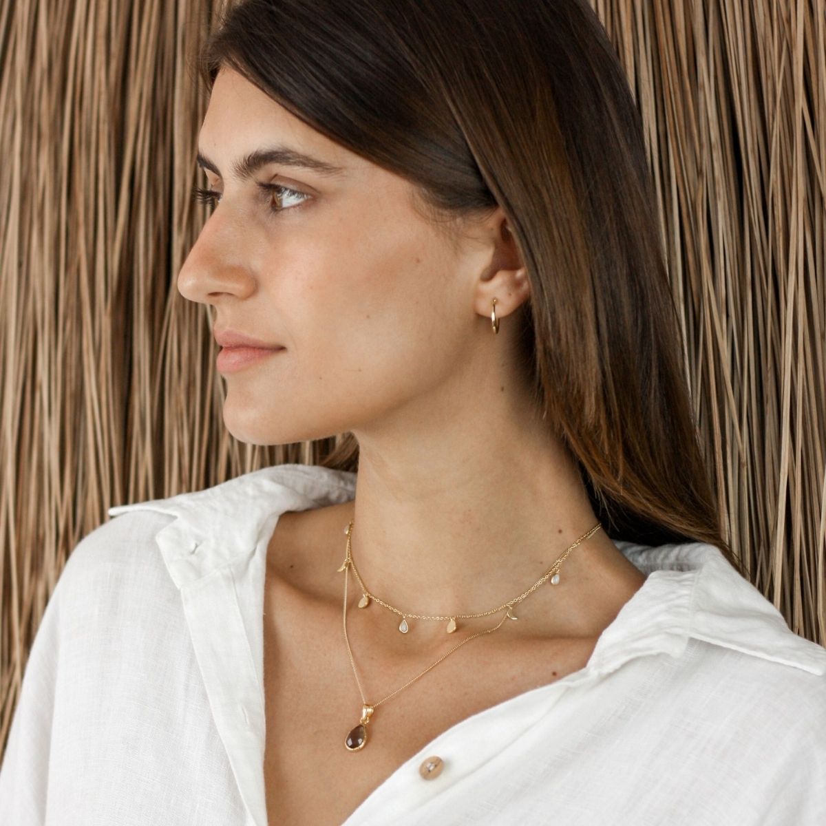 a woman looking to the side wearing two necklaces around her neck