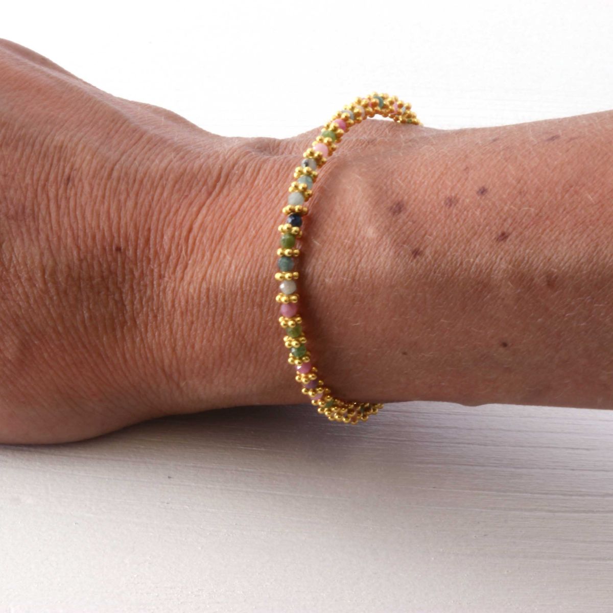 a woman wearing a multi coloured tourmaline bracelet on her wrist