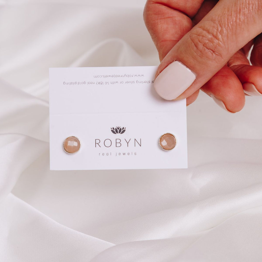 a woman holding a card with peach moonstone studs on 