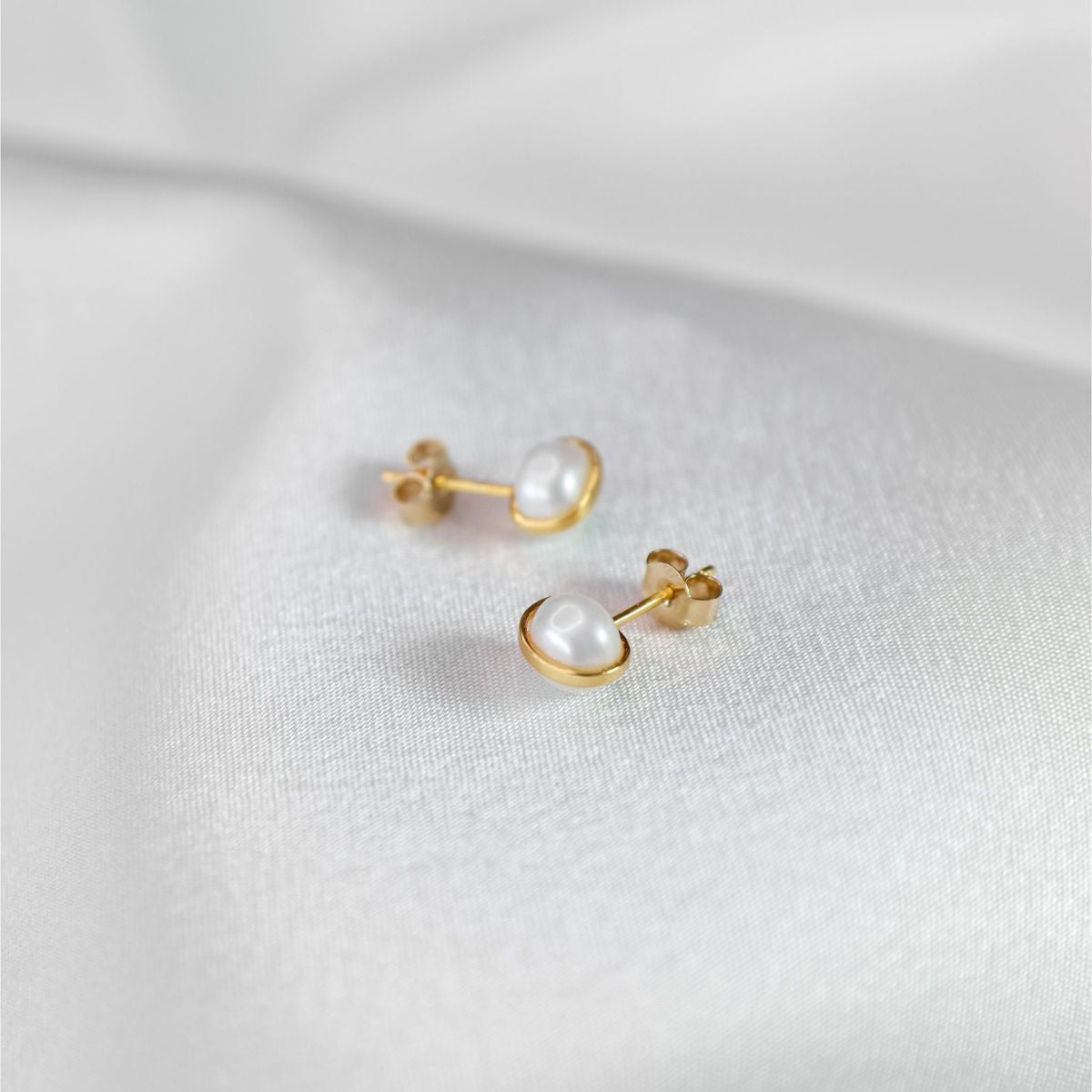 a pair of white pearl earrings on a white cloth