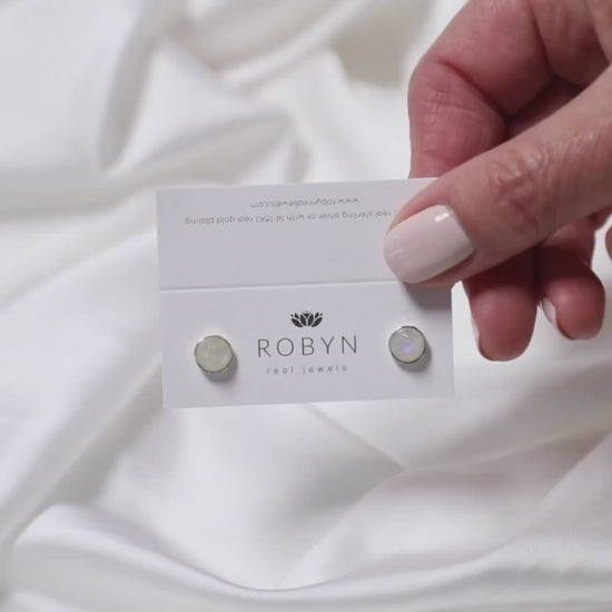 a woman holding a pair of moonstone studs 