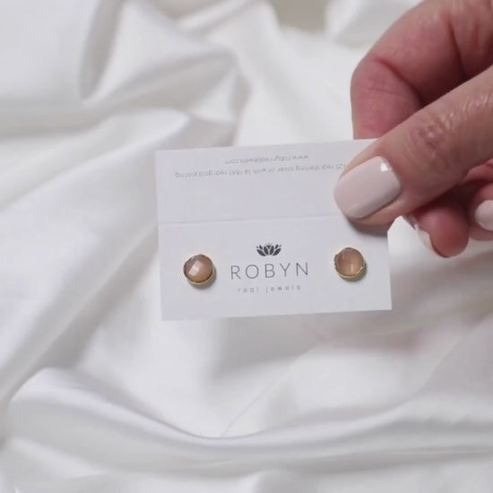 a woman holding a card with peach moonstone studs on