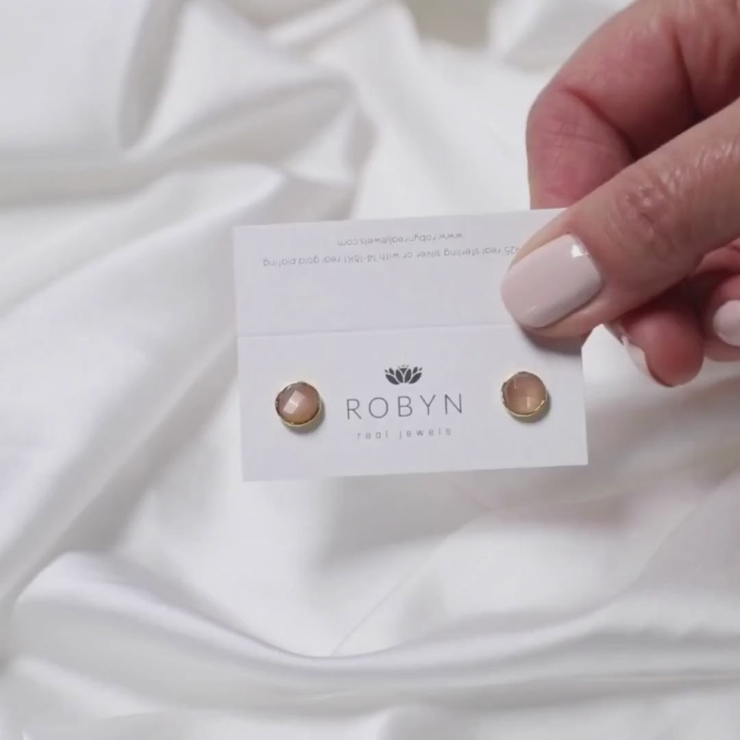 a woman holding a card with peach moonstone studs on