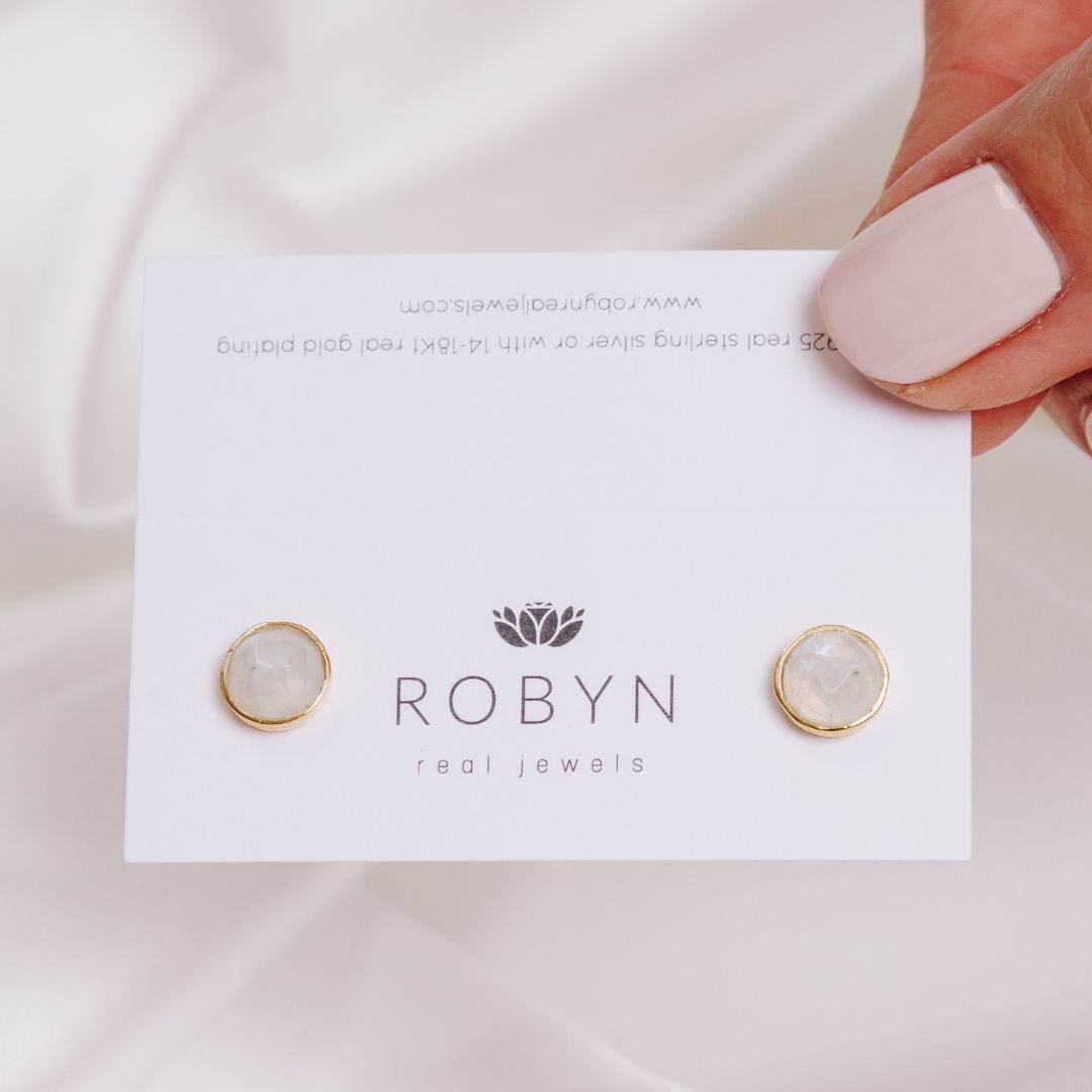 a woman holding a card with moonstone studs 