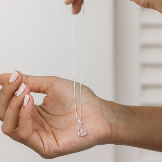 a woman holding a pink pendant necklace in her hand